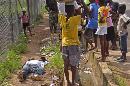 Varios niños rodean a un hombre, izquierda, que cayó al piso mientras caminaba y que presuntamente contrajo el virus del ébola, en la ciudad de Monrovia, Liberia, el martes 19 de agosto de 2014. (Foto AP/Abbas Dulleh)